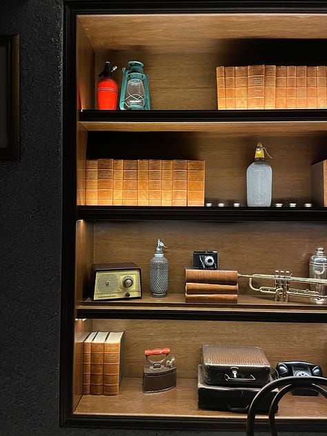 First image: line of suits in a windowcase. Second image: curated bookcase. Third image: a cocktail in a coupe.