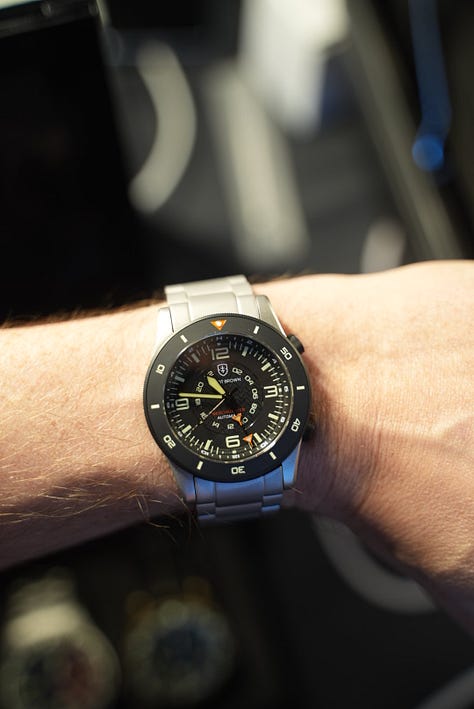 Beachmaster on wrist, with Gem holding a coctail, a display of the watch models made by EB, and a black PVD coated Arne