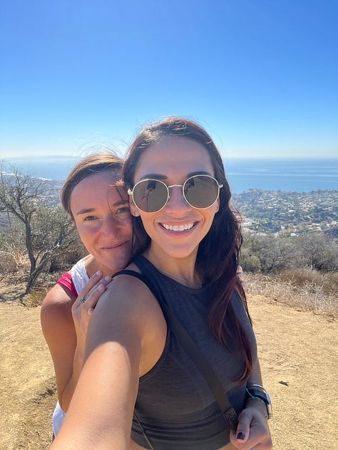 One row of three photos, left to right: Selfie photo of woman holding up her digital camera with sandy, gravelly driveway in the foreground and white one-story buildings in the background; Photo of woman standing in a darkened crevice, on boulders wedged between larger boulders and slabs of rock; Selfie photo of two women smiling atop a hill on a hike overlooking low lying hills that fall away to the Pacific Ocean.