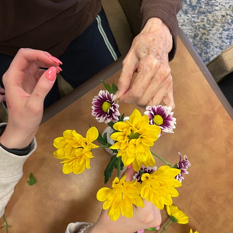 Hands, young and old, arrange bouquets and paint wooden birdhouses together. 