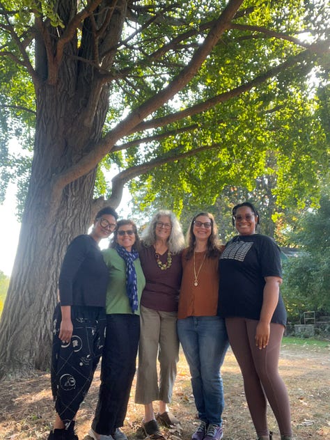 a woman walks into a meadow of trees turning colors, 5 women stand together under a tall tree, a candle and brystals, a hournal on a picnic table, a woman writing in her journal, falling leaves