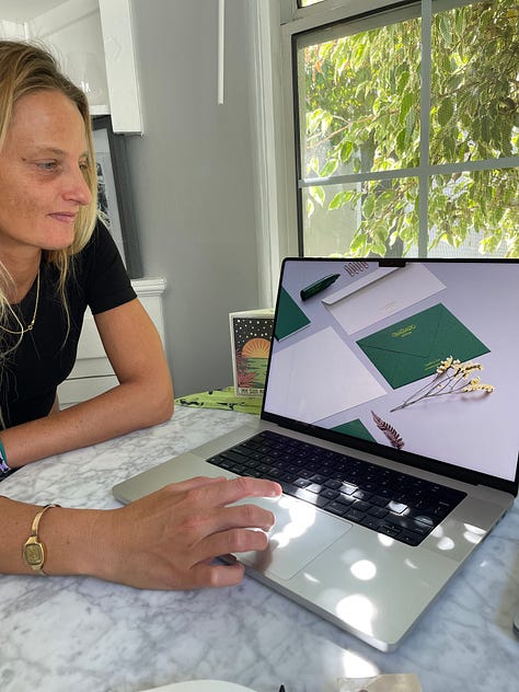 One row of three images, left to right: Woman sitting at dining table presenting her laptop screen showing her creative designs for stationery with bubbles of light on the computer coming through the window in the background; Photo of woman’s back as she holds her digital camera with one hand up to her shoulder, looking off into the desert mountain landscape from atop a trail; Photo of woman cleaning her camera lenses sitting on a bed with sunlight streaming in through the window and an abstract painting hanging on the wall behind her.