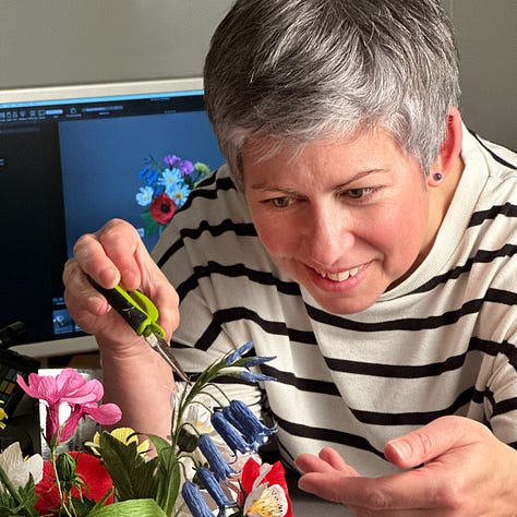 A beautiful arrangement of wildflowers in bright shades of pink, yellow, red, blue and white, presented in a green cabbage leaf mug, against a dark grey background. Two pictures of the author trying not to laugh, or breathe too hard, on the arrangements as she makes the final tweaks!