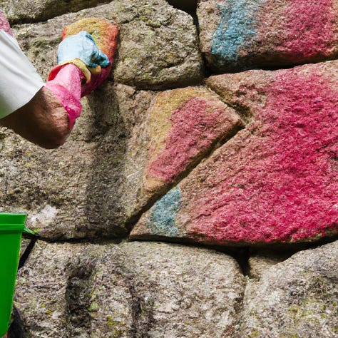 Hands cleaning oil paint off of stone walls