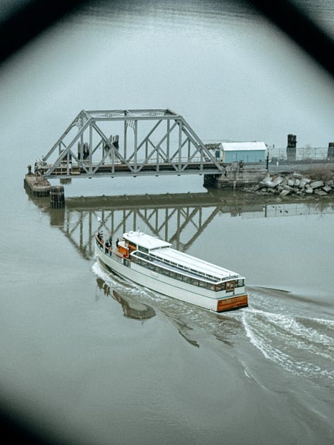 First image: A boat moving through water toward an opening in a gate. Image two: A bookshelf packed with various books. Image three: Overhead view of a wooden serving tray with a burger, cup of ketchup, and fries.