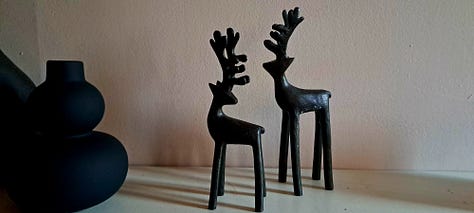 Six photos of stag decorations. 1. cushion with stag head; 2.  2 small black wooden deer ornaments; picture in frame of stag against blue background with message 'Season's Greetings'; white wooden stag figure; two silver stags facing each other with their antlers as candleabra; delicate white ceramic stag tree decoration.