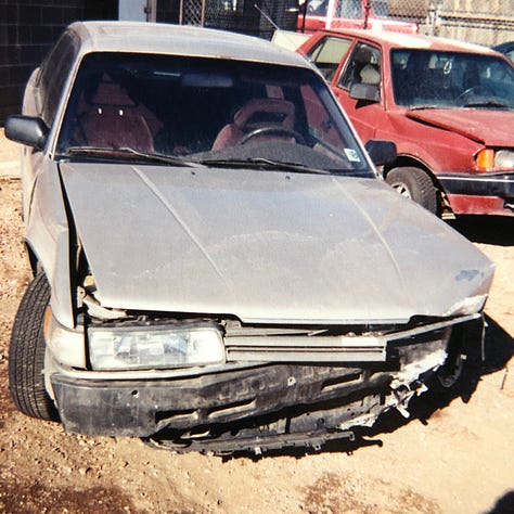 My champagne Mazda 626 lurches cockeyed in the wreck yard with other munched vehicles. The smashed front bumper lies on the ground. The windshield is lanced with cracks. The passenger side is caved in. The drivers side is demolished.