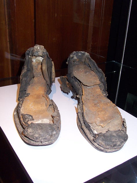 A pair of old shoes, partly decomposed, with patches of leather missing and flaked surface.