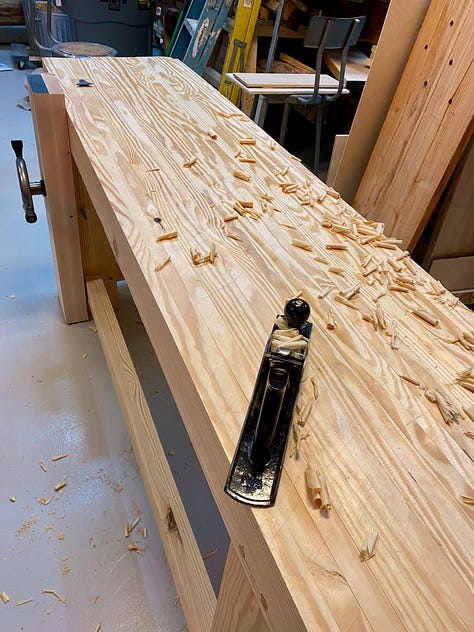My workbench upside down on a table, the vice installed and a hand plane making shavings to flatten the bench top.