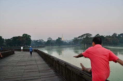 Images of the boardwalk and people exercises in the early morning at Kan Daw Gyi Lake in Yangon. The sun is rising and there is a mist over the water. You can see the golder pagoda Shwe Dagon in the distance.