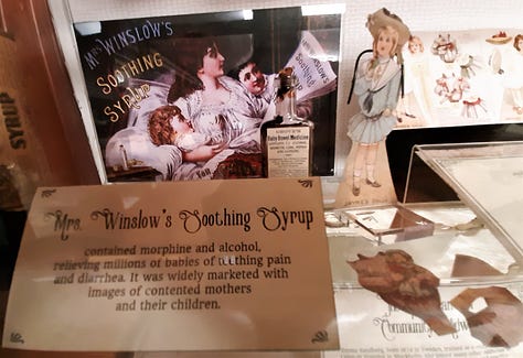 A gallery at the Country Doctor Museum set up as a "sick room" showing a bed and other articles that might be found, including a flower-painted pitcher and basin for washing up, and Mrs. Winslow's medicine advertisement.
