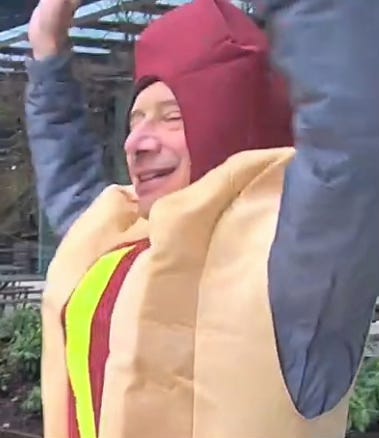 group with signs and singing; sheet cake, dancing man in hotdog suit