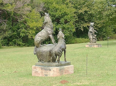 Outdoor sculpture park with metal sculptures of wolves, bears, famous indigenous Americans and a park bench. Flat metal sculptures of bison resemble a small herd across a prairie field.