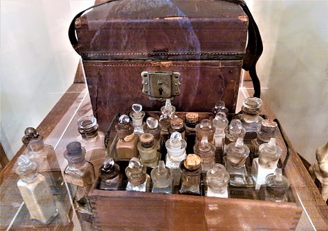A skeleton that was used for teaching, along with a case with many vials of medicines in front of it and a long tube holding original handmade pills.