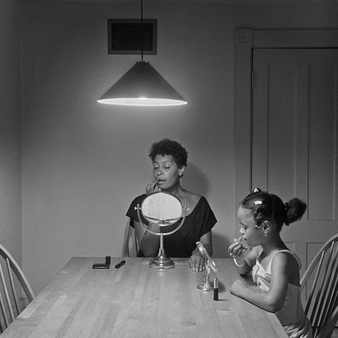 1-9) All images are black and white, and involve a table, as well as a few chairs, and an overhead light. 1) A black woman is seen playing cards by herself. 2) A black woman is seen holding her head in her hands, while reading a book. There is a child sitting to her right, writing. 3) A black person is standing at the end of the table, looking into the camera. 4) A black woman is looking at herself in a tabletop mirror, while a child is playing to the right of her at the table. 5) Three people are sitting at the table, and appear to be playing a game or laughing. 6) A black woman is seen looking at herself in a tabletop mirror. 7) A black woman is sitting on the left side of the table, with her hand under her chin. There is a black man at the end of the table, reading the newspaper, with his hand resting on his neck. 8) Two black people are seen kissing/embracing. One is sitting at the end of the table, and the other person is behind them. 9) A black woman is seen with her head laying back on the table, with her hands in her hair.
