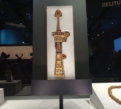 From left: Necklace made of gold nuggets and jade ornament, gold and genstone-encrusted dagger sheath, and a small cobalt blue drinking glass