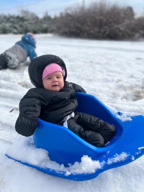 Young child playing in snow, baby on blue sled. 