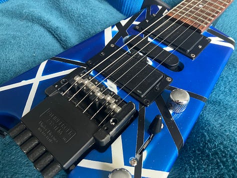 An image gallery showing a headless guitar being stripped down, sanded, repainted, and reassembled. By the end, it's blue with black and white stripes, and looks extremely shiny.