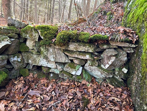 A stone construction in the woods against a cliffside.