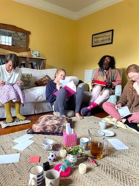 L-R: three white women and one Black woman sit on sofas and the floor writing in journals, with tissues, herbs and a jug of herbal tea in the foreground. A group of nine women stand in a circle on the lawn of a farmhouse, in the background. 10 women eating lunch around a farmhouse style table, with floral arrangements in the centre. Three women crouch on the wooden floor of a barn, their backs to us, lighting candles. In the foreground is a floral mandala arrangement. Four women clamber down a steep coastal path to the beach