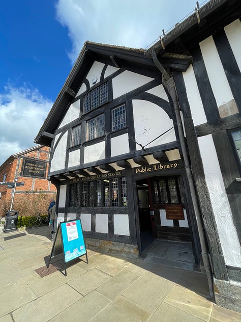 Old Tudor house with wood beams, old windows against a blue sky; swans and ducks on the River Avon; The old public librabry in white and wood Tudor style; The Royal Shakespeare Theatre; The Pen and Parchment pub with sign hanging, windows and flowers 
