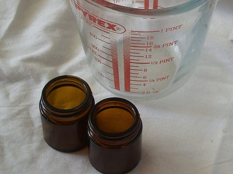 A double boiler containing oils and marigold petals and examples of brown glass ointment jars