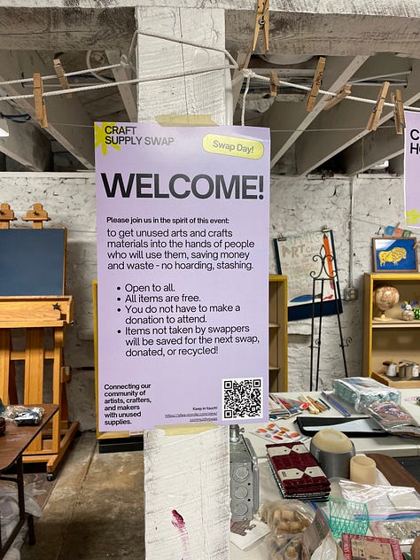 Swappers in a basement space that has filled up with tables and craft materials, clear jars with votes on having the swap again, and a Meadowlark Guide Co coffee mug from a friend who helped arrange materials.