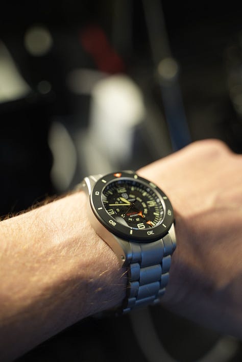 Beachmaster on wrist, with Gem holding a coctail, a display of the watch models made by EB, and a black PVD coated Arne