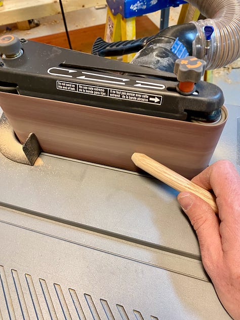 Holes bring drilled, via a drill press, into the bench legs; overlapping drawbore holes; sanding drawbore pegs; and then waxing and temporarily inserting them into the bench base.
