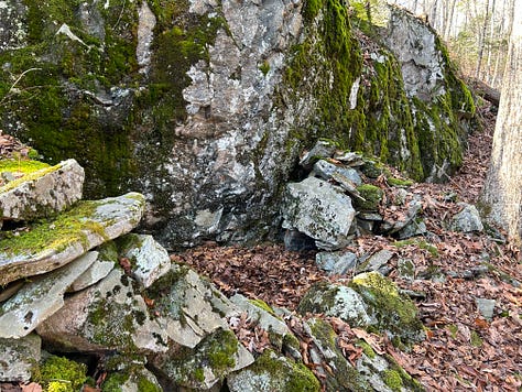 A stone construction in the woods against a cliffside.