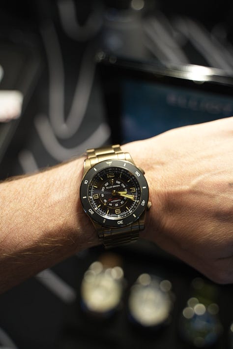 Beachmaster on wrist, with Gem holding a coctail, a display of the watch models made by EB, and a black PVD coated Arne