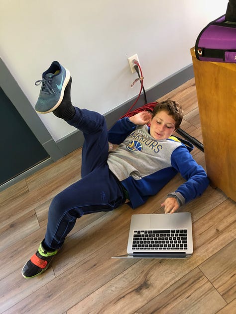 kid sitting at a desk doing math, kid lying on the floor with a laptop doing situps, three kids holding a microphone and recorder, interviewing a stuffed bear