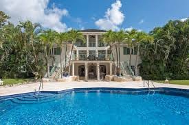 Elegant Villa Aliseo in Barbados’ Sandy Lane Estate, surrounded by lush tropical gardens, featuring an expansive swimming pool, private tennis court, and sophisticated outdoor dining area on the large terrace. The luxurious nine-bedroom villa offers a perfect blend of privacy and indulgence.