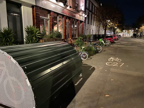 A variety of pictures of London streets at night. One shows a bus stop with people waiting at it. Another a bike locker and other bike parking. Another shows a van and car for hire. The rest show street scenes with Georgian town houses and empty streets lit by street lights