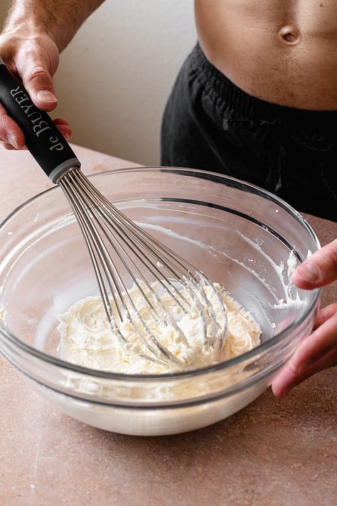Making vegan cream cheese frosting in a glass bowl with a whisk on a red counter