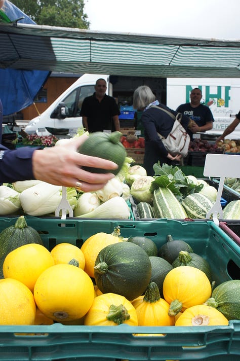 Wimbledon Farmers Market; fisherman with customer, customer with summer squash, cake stall, child with soft fruit, crabs, cherries, customer & basket, beans & aubergines, customer with dairy