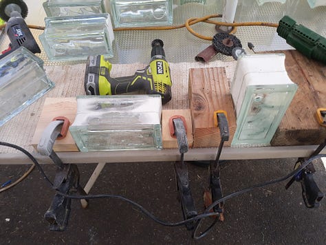 From left to right; hole bore with reservoir and seals, a workstation set up for multiple blocks (16 of them), clamps and wooden blocks, a drill with wire wheel for burnishing off powder coating,coarse sandpaper for deburring hole and a finished block. [Not shown is a drill press, dust mask and eye protection]