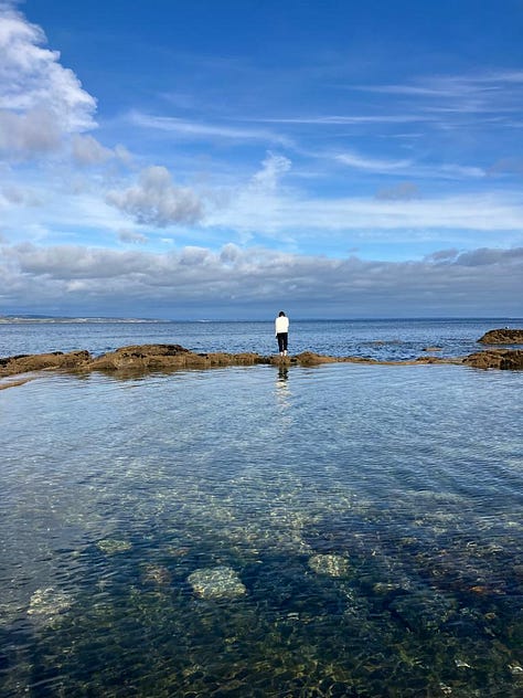 Woman with her feet in the water, woman looking out to sea, woman in the water.