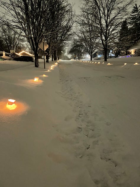 9 images in a gallery: an infrared sauna lit pink, luminaries on a snowy street at dusk, a candle and legs crossed on a yoga mat, a 3 year old boy in a blue coat plays in the snow, a 40 year old windswept woman walks by lake michigan and a red lighthouse, seasonal hand cream and chapstick, a seasonal soup in a red enamel pot, hot chocolate with marshmallows, and a cozy massage table