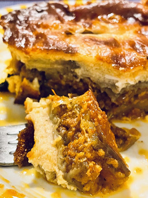 Close-up of a serving of Moussaka, showcasing its creamy béchamel topping and flavorful layers of eggplant, meat, and spices.