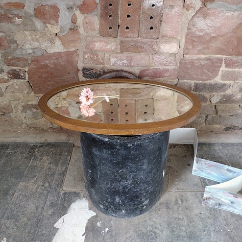 Images of artworks in a dilapidated room, plaster and lath crumbling away from the walls, and artist hanging her work on the wall, a pink flower artfully placed on a mirror and photographed to show reflections of other artworks in the mirrored glass