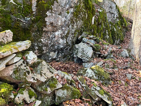 A stone construction in the woods against a cliffside.