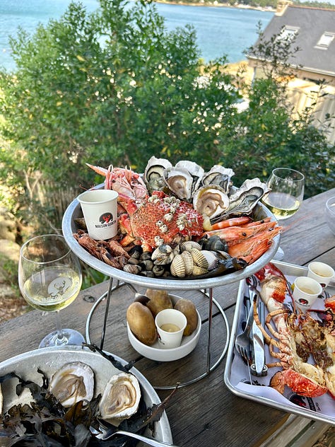 an evening harbor filled with boats; restaurant sign offering oysters and wine, a seafood platter; a breakfast picnic basket