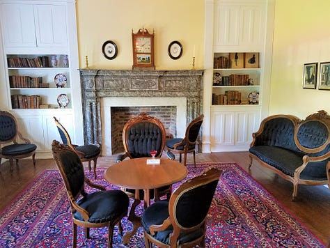 The Dickson Williams Mansion, a brick building with a white porch; the parlor, showing a round table surrounded by black chairs on a red oriental rug in front of a fireplace; the kitchen area, showing original north carolina furniture; bedrooms of the house, along with a portrait of General John Hunt Morgan sitting in a chair in a black coat with tall black boots; and the bed where he spent his last night. 