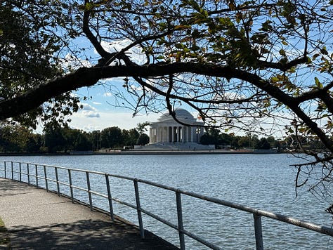 A group of three people posing for a photo. The middle person is wearing a plaid shirt, while the person on the right wears a maroon shirt and glasses.  A plate with two large pancakes topped with powdered sugar and what appears to be blueberries. There's a side of whipped butter and syrup served on the side. A scenic view of the Jefferson Memorial from across the water, framed by tree branches on a clear day. A set of blue mugs with white writing that says, “I cannot live without books,” attributed to the Thomas Jefferson Memorial. A stone wall with a famous quote engraved on it, "The only thing we have to fear is fear itself." This quote is from Franklin D. Roosevelt, suggesting this is part of the FDR Memorial in Washington, D.C. A candid moment of the same group from the top-left photo, where one person is handing an object (perhaps a book or certificate) to another person. The setting appears informal, possibly part of a casual ceremony or presentation.