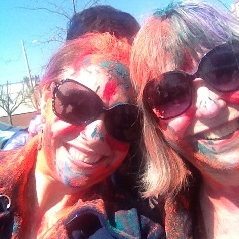 The author and her mother covered in a rainbow of thrown chalk dust, head-on-shoulder at the Fourth of July, and the obituary photo with her favorite turquoise Chihuly blown glass reeds behind her. Always with huge, matching smiles. Always.