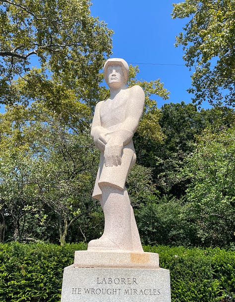 large limestone sculptures in an outdoor sculpture garden against a blue sky depicting a laborer, a scientist, and a poet