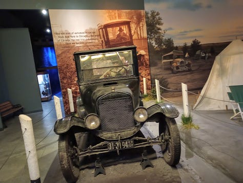 Photo of car driving through extremely deep mud, Model T car from 1920s,Info panel, Model T with mural of motor court behind, mural and tableau of motor court cabins