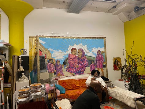 Blue goddess statue, working class woman and her daughter both in pink hijabis, gold-colored goddess icon with orange detail.