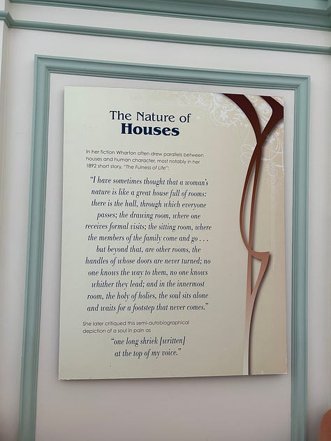 1: Informational display titled "The Nature of Houses" with text and decorative motifs. Transcribed Text: The Nature of Houses In her fiction Wharton often drew parallels between houses and human character, most notably in her 1892 short story, "The Fulness of Life": "I have sometimes thought that a woman’s nature is like a great house full of rooms: there is the hall, through which everyone passes; the drawing room, where one receives formal visits; the sitting room, where the members of the family come and go . . . but beyond that, are other rooms, the handles of whose doors are never turned; no one knows the way to them, no one knows whither they lead; and in the innermost room, the holy of holies, the soul sits alone and waits for a footstep that never comes." She later critiqued this semi-autobiographical depiction of a soul in pain as "one long shriek [written]  at the top of my voice." 2: Elegant library with dark wood and floor-to-ceiling bookshelves, ornate decorative features, antique furniture, and large windows. 3: Framed image of Edith Wharton sitting at a desk with a text quote beside her portrait. Transcribed Text: Edith Wharton staged publicity photos to give the impression she wrote at a desk, but she really did most of her writing in bed: “She would have her writing board perilously furnished with an ink-pot on her knee, the dog of the moment under her left elbow and the bed strewn with correspondence, newspapers and books.” Gaillard Lapsley (1871-1949), friend of Edith Wharton. 4: Picture of an elegant dining room with a round table covered by a white tablecloth, set with crystal glasses and candlesticks. The floor is carpeted in a beige, woven pattern. Under the table, a small, fluffy dog with long hair is lying on a leopard-print cushion. 5: Weathered gravestone in a forest with the inscription "Our Sweetheart Modele, Died Jan 5 1914." 6: Poster with a photo of an interior hallway and text about the purpose of doors. Transcribed Text: Above all, privacy For Wharton, doors created privacy as well as beauty. Inspired by European houses, the main floor of The Mount is in a style called enfilade. All rooms open up to the next room and doors are lined up to allow vistas from one room to another. “…the main purpose of a door is to admit, its secondary purpose is to exclude.”  Edith Wharton, The Decoration of Houses, 1897 7: Photograph depicting white and pink flowers, which circle around a small man-made pond. In the background, a manicured garden is visible. 8: An open spiral notebook with handwritten notes on the right page. Transcribed Text: YES AGREE! More fake dogs please! yes ma'am! yess! please!! Edith has such a slay style! Love her work in both design, art & literature! ~ Kloey More fake dogs plz! ❤️[heart] 9: Text on a beige wall about Edith Wharton's writing style. Near the left side, the text reads, "The innermost room..." in a larger, bold serif font. Below this, there is a paragraph in a smaller, sans-serif font describing the writing style of Edith Wharton.  Transcribed Text: "The innermost room..." Edith Wharton did not write happy endings. Her stories feature the lost chance; her characters yearn for someone to join them in that innermost room of the soul. Whether Wharton achieved that in her own life, and with whom, is a story as mysterious and captivating as any of her fiction.